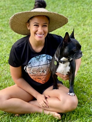 Pua Pakele of RBL Media sitting outdoors on the grass with her dog