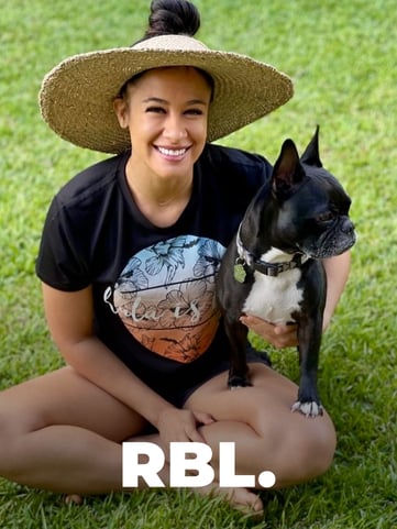 Pua Pakele of RBL Media sitting outdoors on the grass with her dog